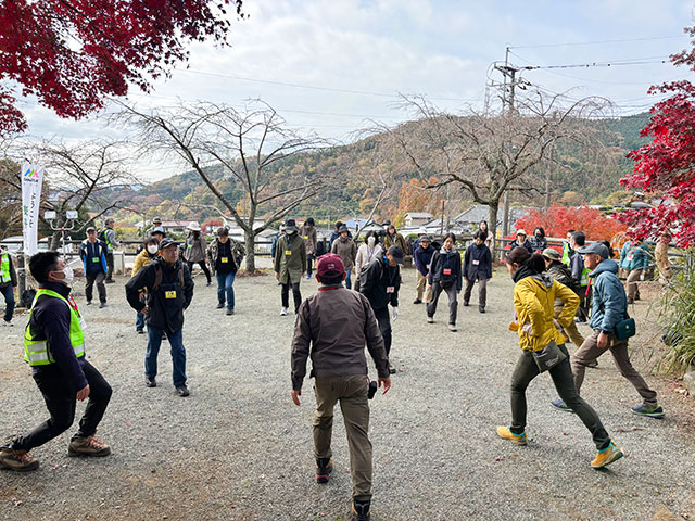 公園でストレッチする参加者たち。周囲の木々は紅葉している